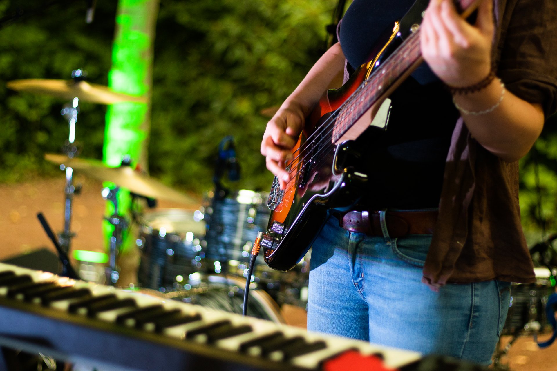 Im Vordergrund ist ein Keyboard zu sehen, links daneben ein Schlagzeug. Ein Mensch (nur der Oberkörper ist zu sehen) spielt auf einer E-Gitarre.