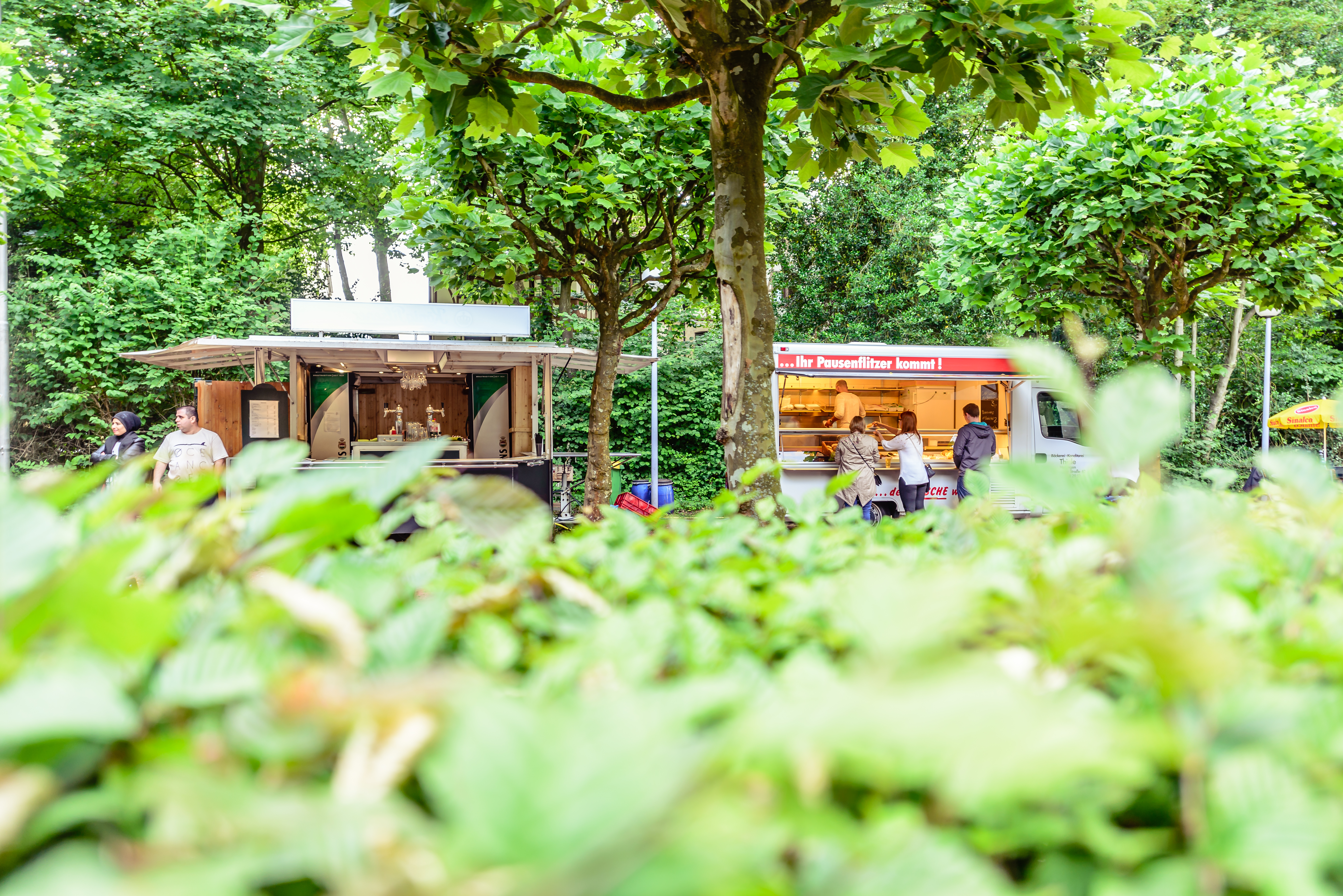 Blick auf zwei Foodtrucks im Biergarten der Freilichtbühne Wattenscheid. Grüne Büsche im Vordergrund.